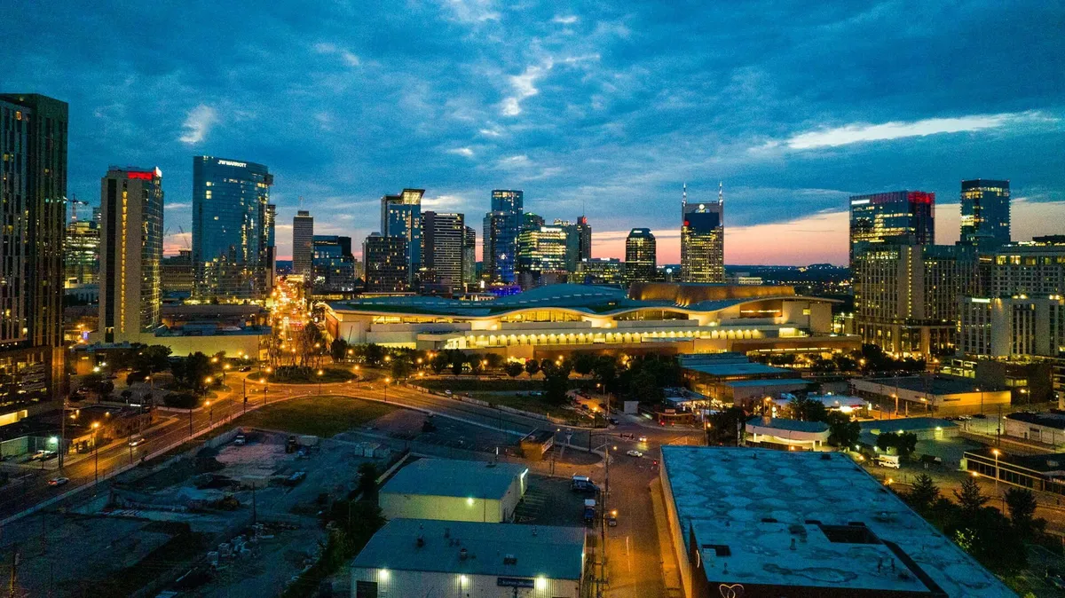 This exterior image captures the Nashville city skyline with the distinct convention center in the foreground, illuminated by street lights and surrounded by a bustling urban environment. The dynamic view contextualizes the property’s central location and proximity to major business venues.