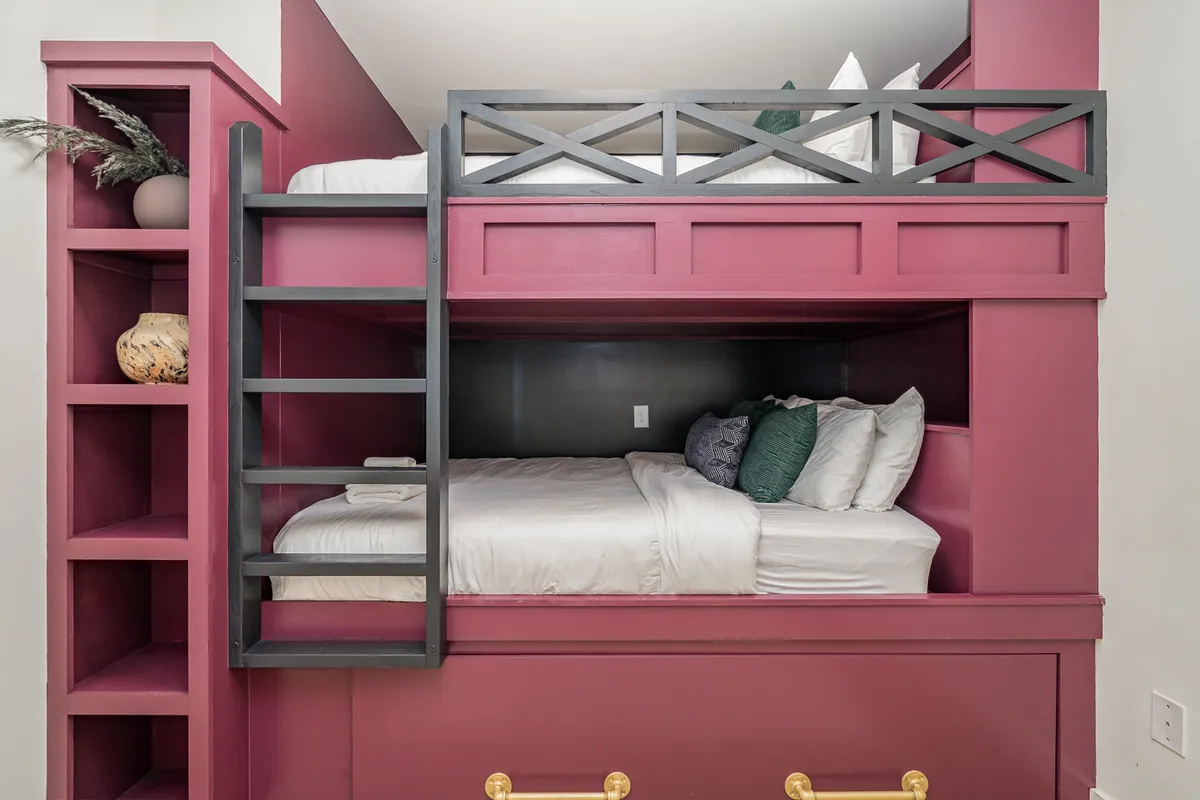 A playful and inviting room featuring a bunk bed, decorative shelving, and colorful cushions. The arrangement offers flexibility for families or groups, maximizing sleep capacity while maintaining a cheerful, modern look.