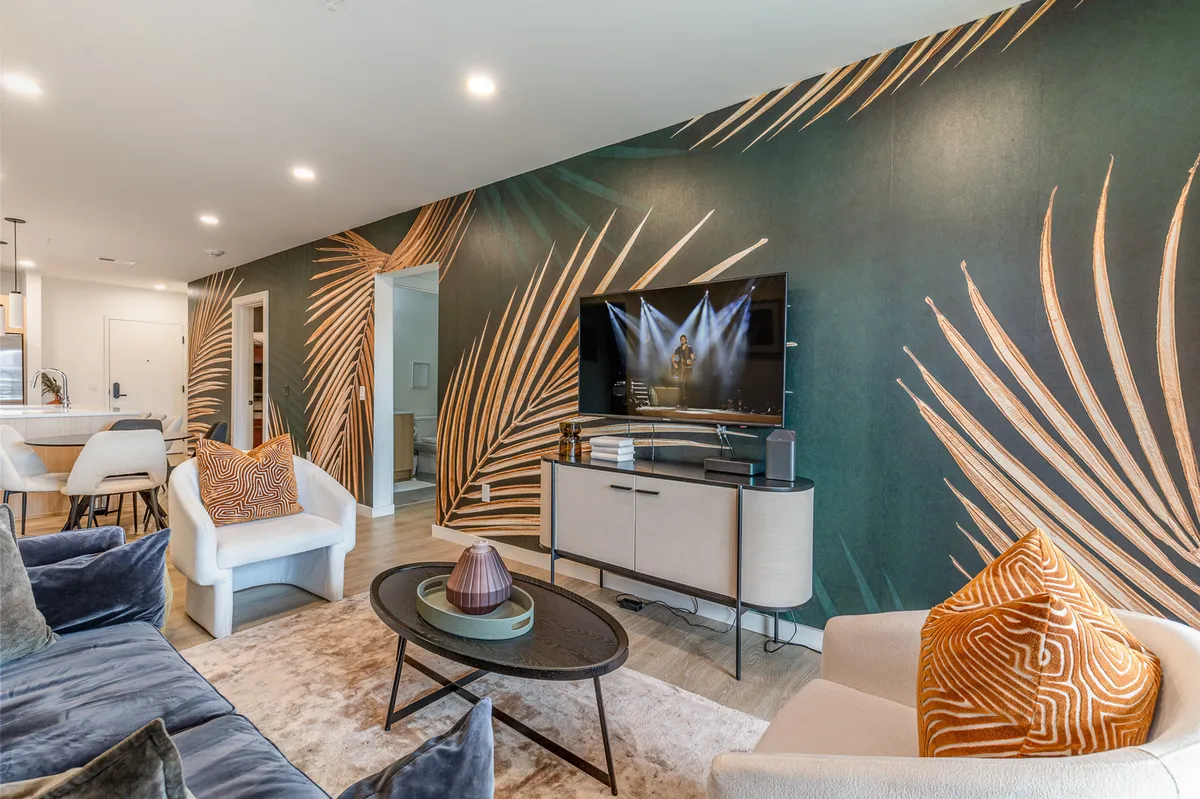 A stylish lobby or common area featuring a large tropical leaf mural, a flat-screen TV, a chic coffee table, and decorative cushions. The space is designed for relaxation and social interaction, blending modern comfort with a welcoming ambiance.