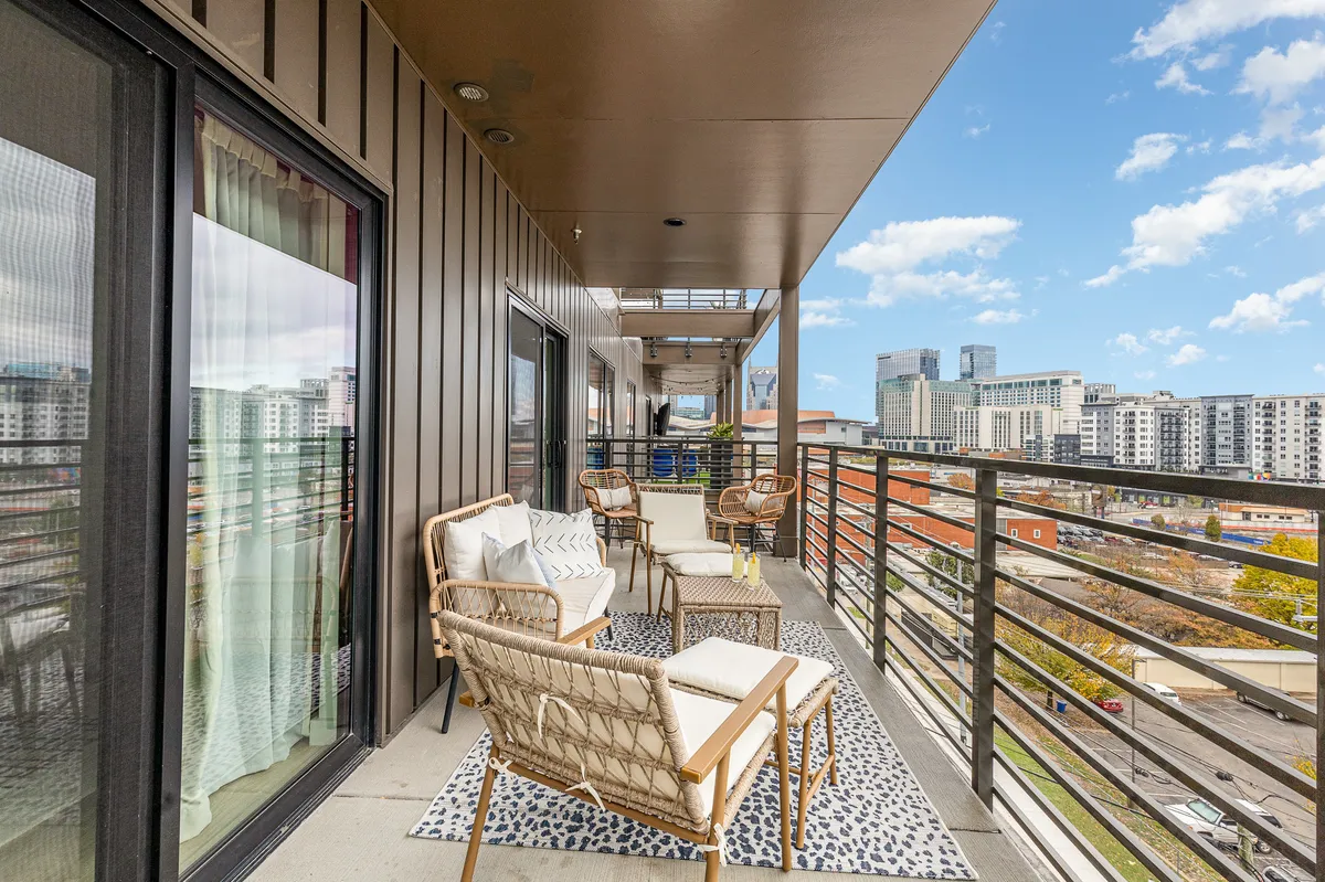 A rooftop lounge area with comfortable balcony seating, a decorative rug, and panoramic views of the city skyline, ideal for sunset gatherings or relaxed mornings.