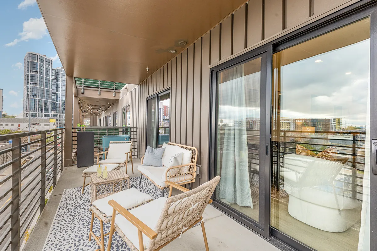 An exterior view from the balcony shows inviting seating, a decorative rug, and sweeping urban views. The tranquil, urban vibe is perfect for enjoying morning coffee, evening drinks, or simply soaking up Nashville's cityscape.
