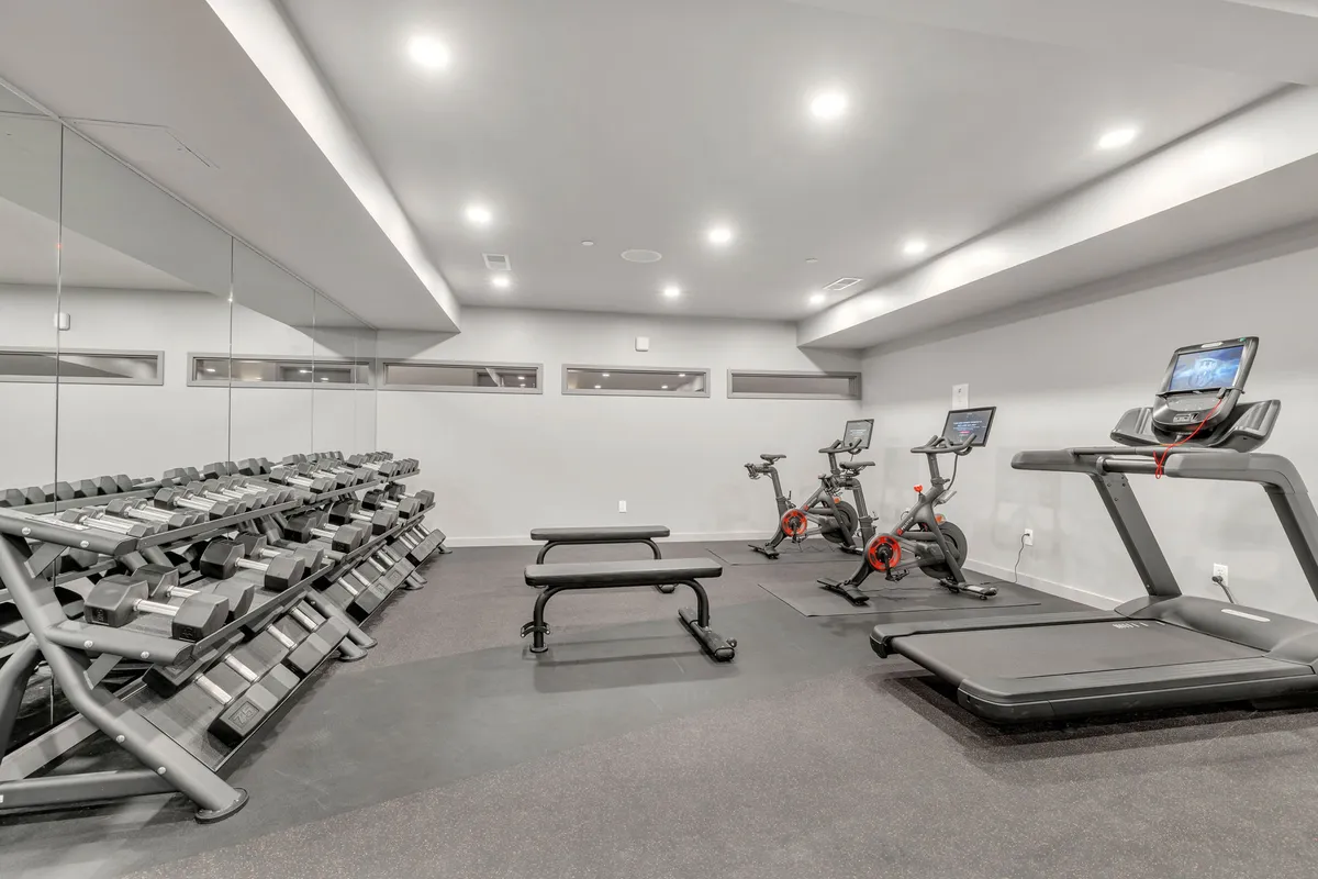 An interior image of a well-equipped gym featuring weight racks, treadmills, stationary bikes, and benches, set in a modern, motivational atmosphere ideal for morning workouts or post-meeting stress relief.