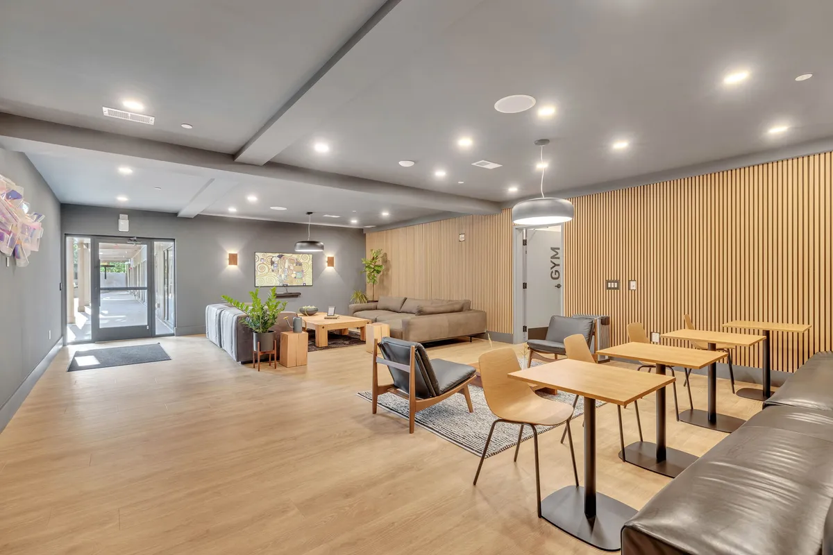 A stylish, spacious lounge with modern sofas, dining tables, decorative wall art, and plant accents, offering a welcoming environment for both work and relaxation. The space is ideal for quiet work sessions, informal meetings, or unwinding after a busy day.