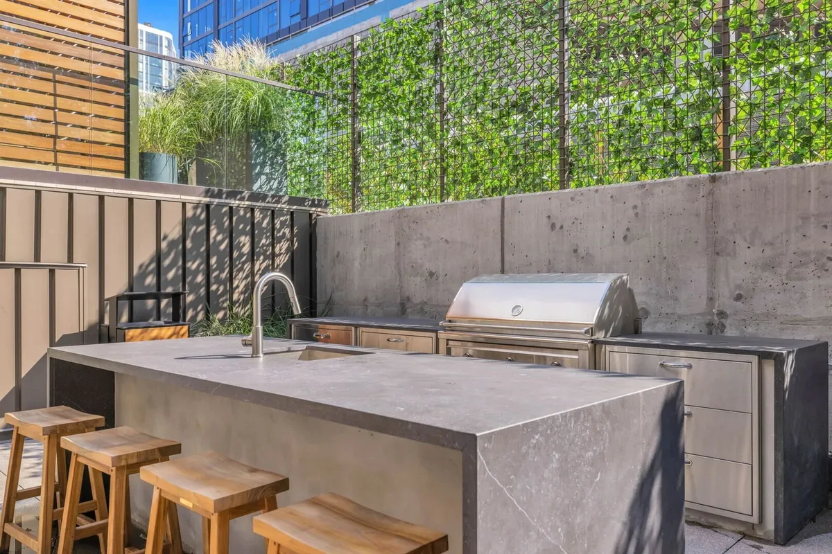 An inviting outdoor kitchen and bar area with bar stools and a lush green wall. The space is designed for social gatherings, festive celebrations, and relaxed meals with friends or family in a stylish setting.