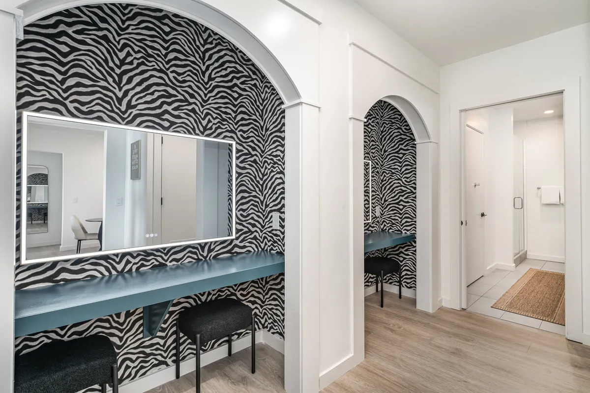 The image showcases a vibrant vanity area with zebra-patterned wallpaper, a mirrored vanity, blue countertop, and stylish seating. The atmosphere is energetic yet playful, making it an ideal spot for pre-event or daily routines.