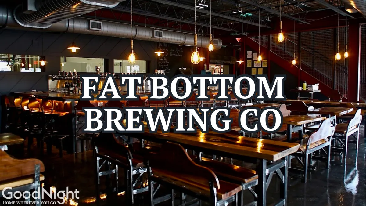 A lively interior of a brewery or bar with long communal wooden tables, a central bar area, and warm lighting. People are gathered for craft beer tastings, meals, and conversation, reflecting a vibrant social scene.